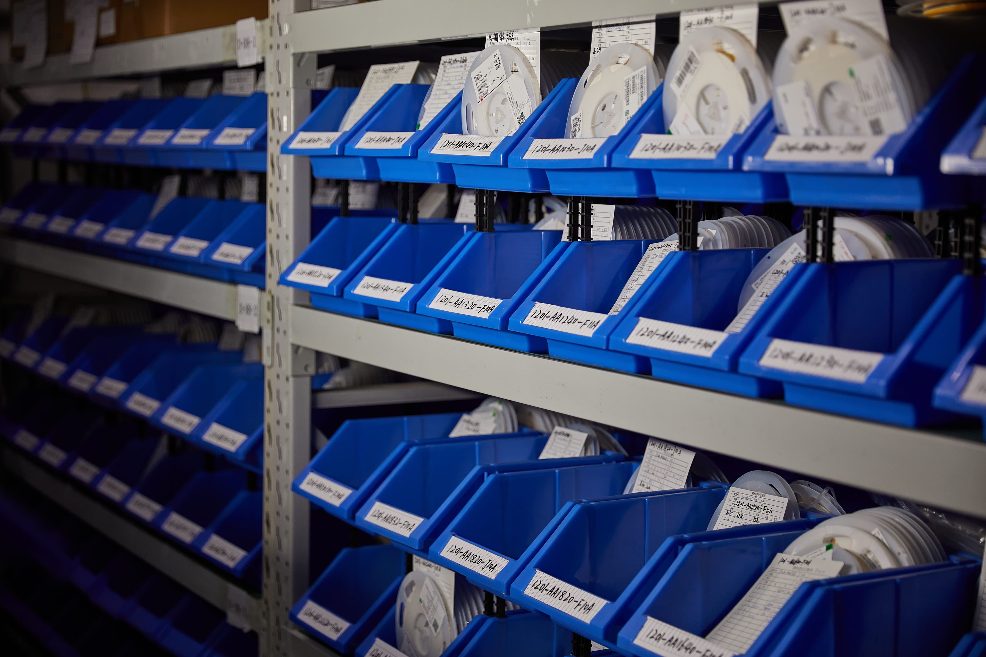 Labeled reels of electronic components stored in blue inventory bins.